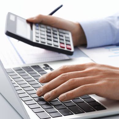 Eine Hand tippt auf einer Tastatur, während die andere einen Taschenrechner hält.