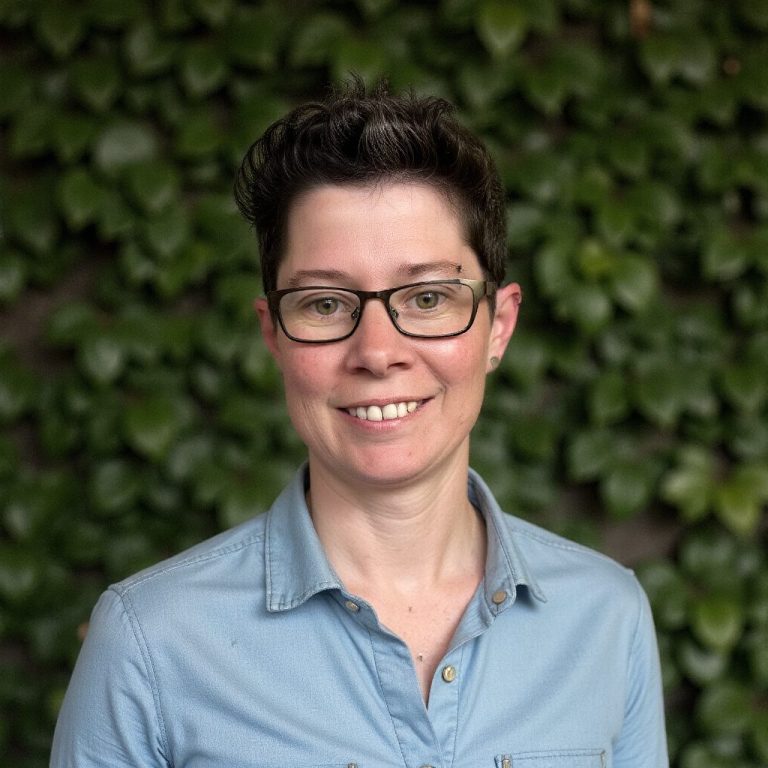 Person mit Brille und kurzen, dunkelbraunen Haaren vor einer grünen, bewachsenen Wand.